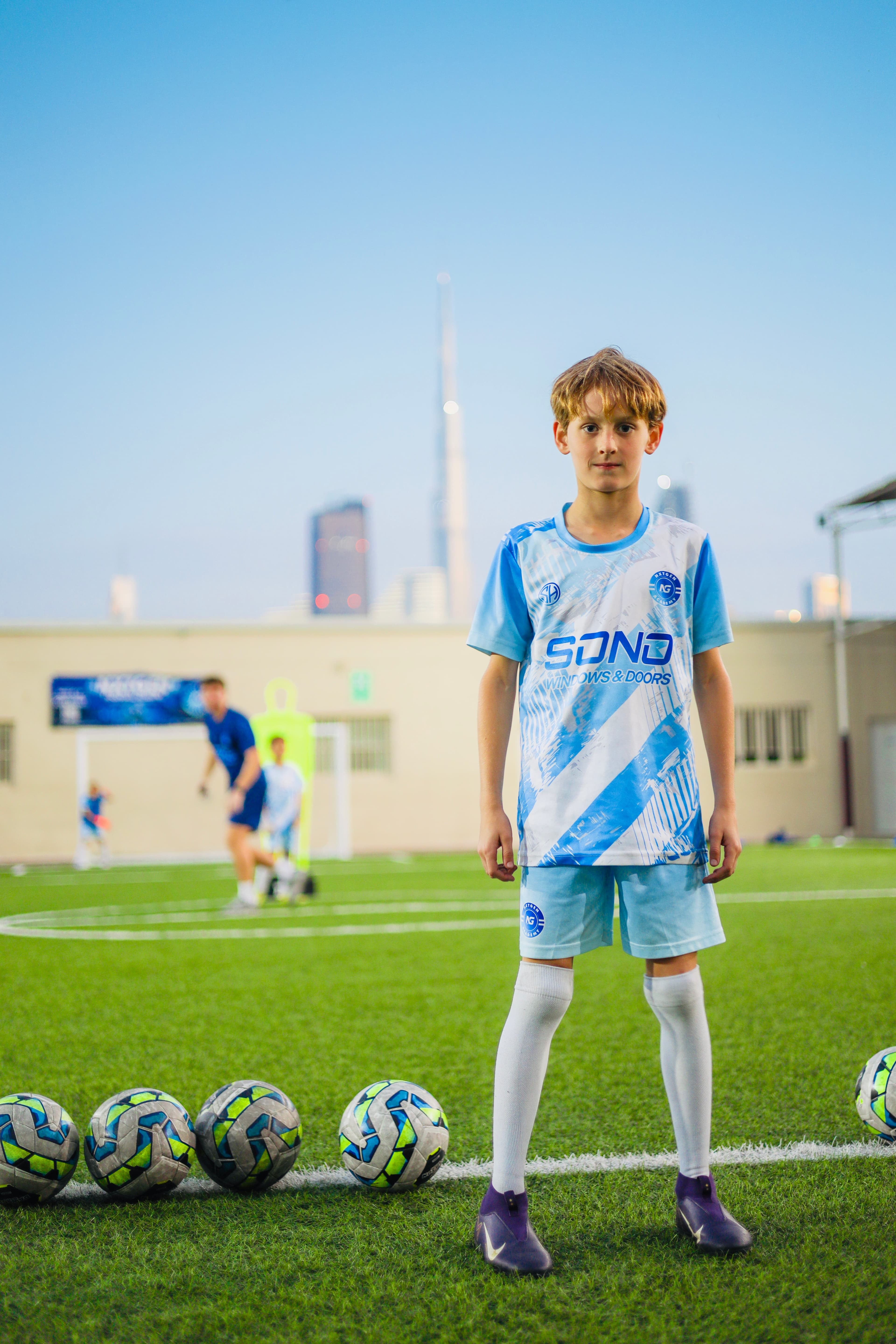 A NXTGEN player stands on the pitch with footballs laid out in front of him.