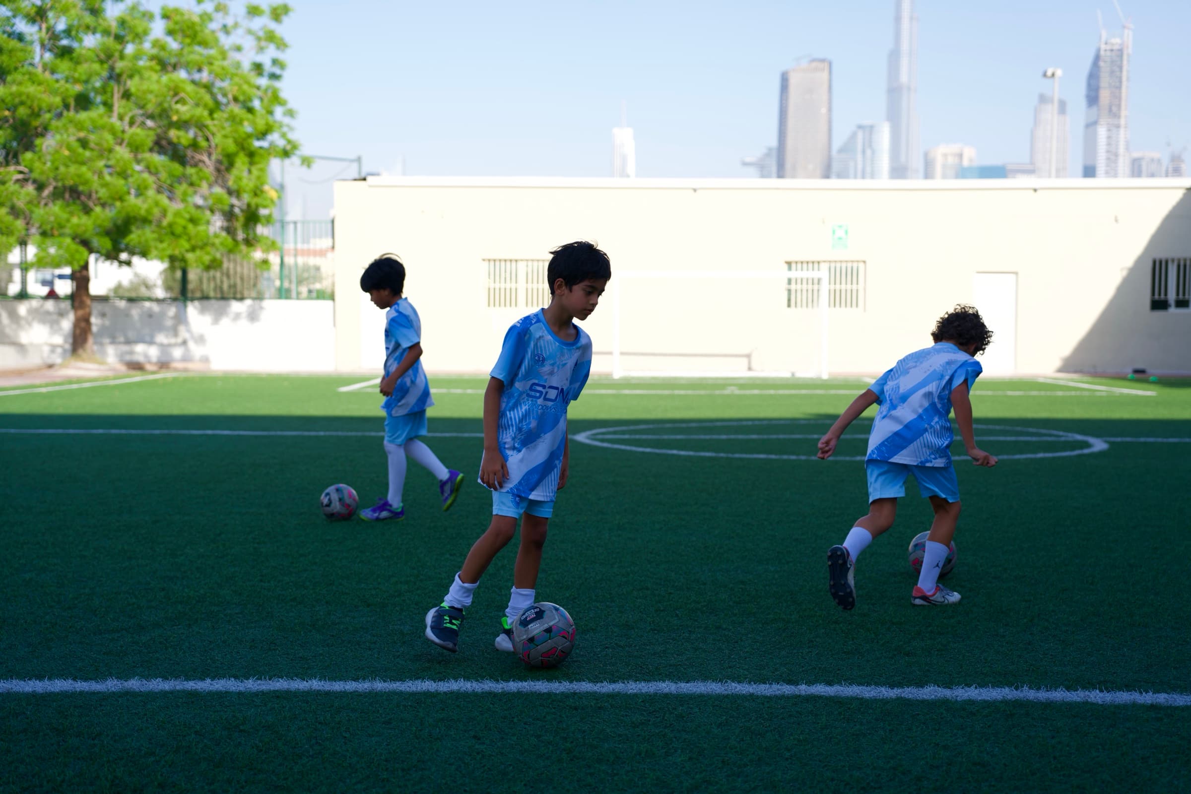 Three young NXTGEN Academy players train with footballs on the pitch.