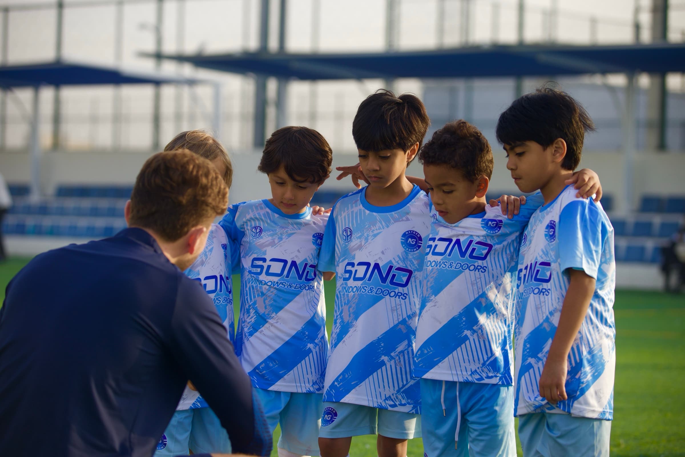 A group of NXTGEN Pre-Squad players listen together during a coaching session.